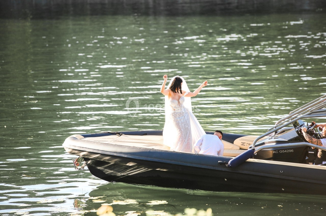 Une femme en robe blanche se tient debout sur un bateau au milieu d'une étendue d'eau calme.