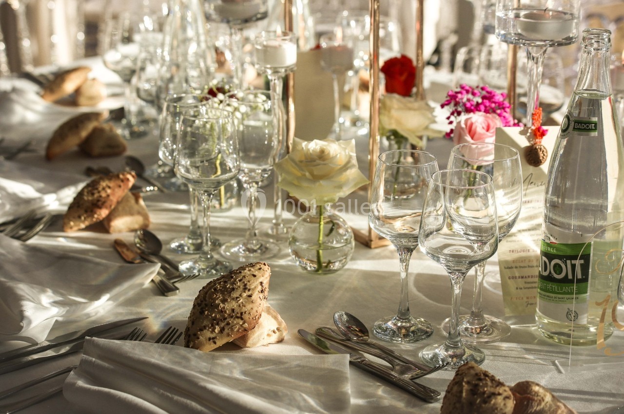 Table élégamment dressée avec verres, couverts, fleurs et pains, éclairée par une lumière naturelle douce.