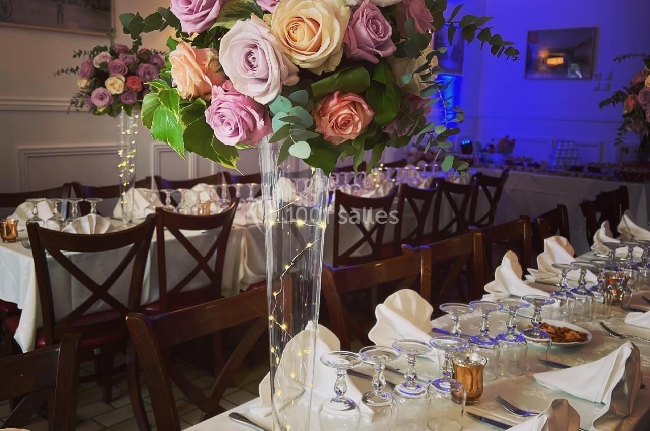 Centre de table floral avec roses pastel et feuillage, posé sur une table dressée pour un repas festif.