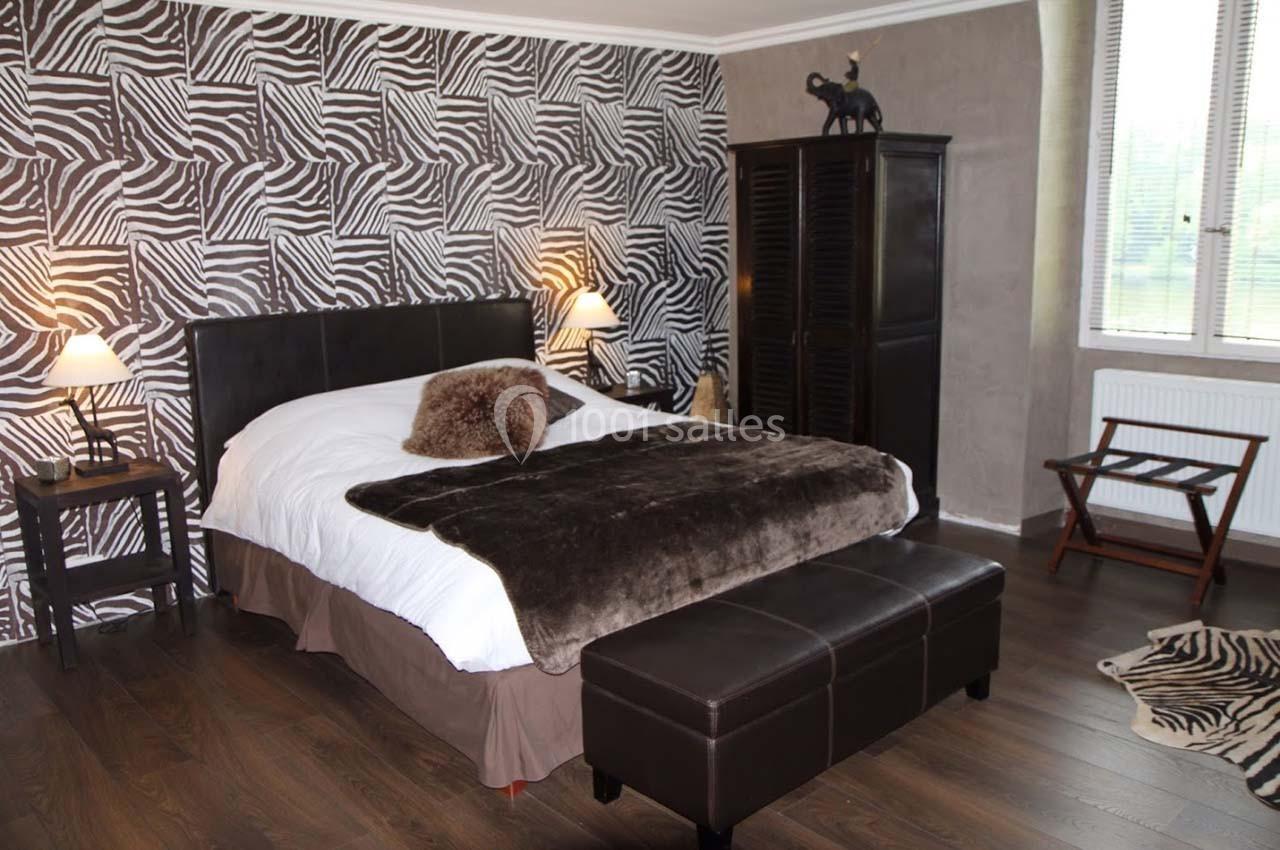 Chambre avec lit double, couvre-lit en fourrure, murs à motif zébré, mobilier sombre et lumière tamisée.