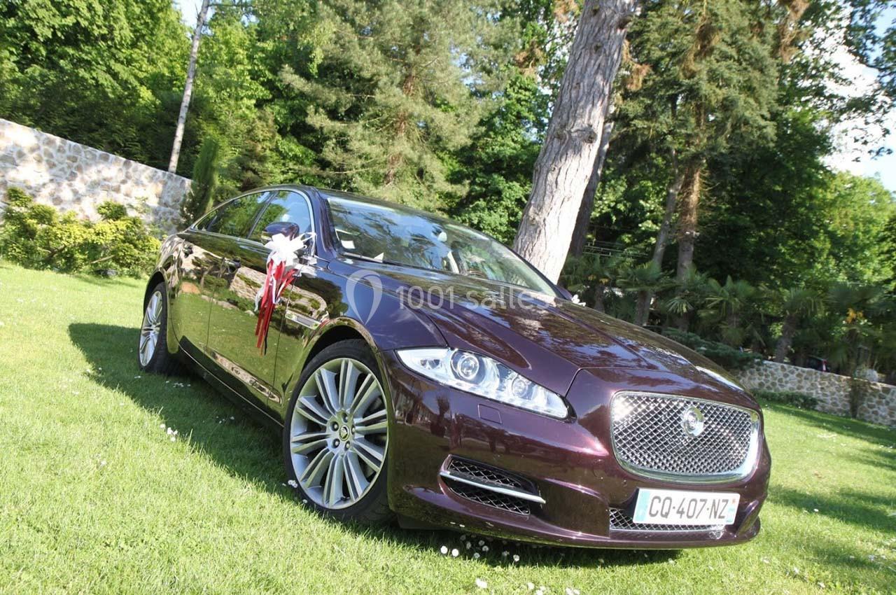 Voiture de luxe violette décorée pour un événement, stationnée sur une pelouse entourée d'arbres et d'un mur en pierre.