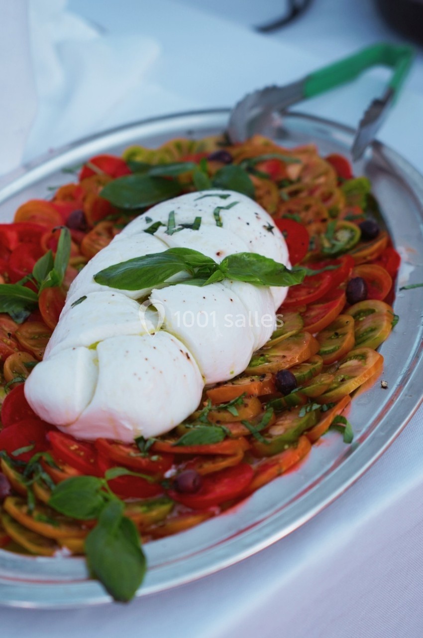 Assiette de mozzarella tressée sur un lit de tomates colorées, olives et basilic, servie sur un plateau argenté.