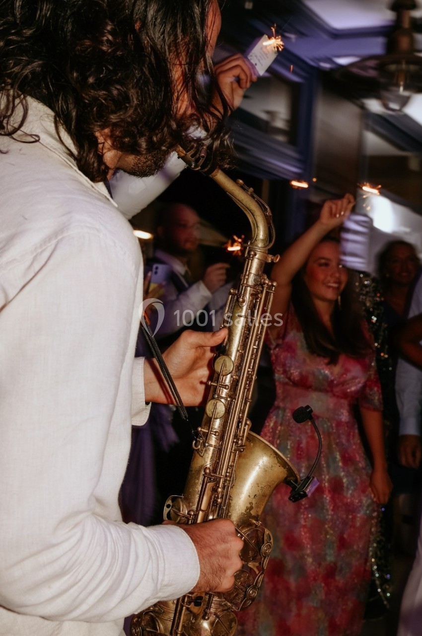 Un musicien joue du saxophone lors d'une fête animée, entouré de personnes tenant des cierges magiques.