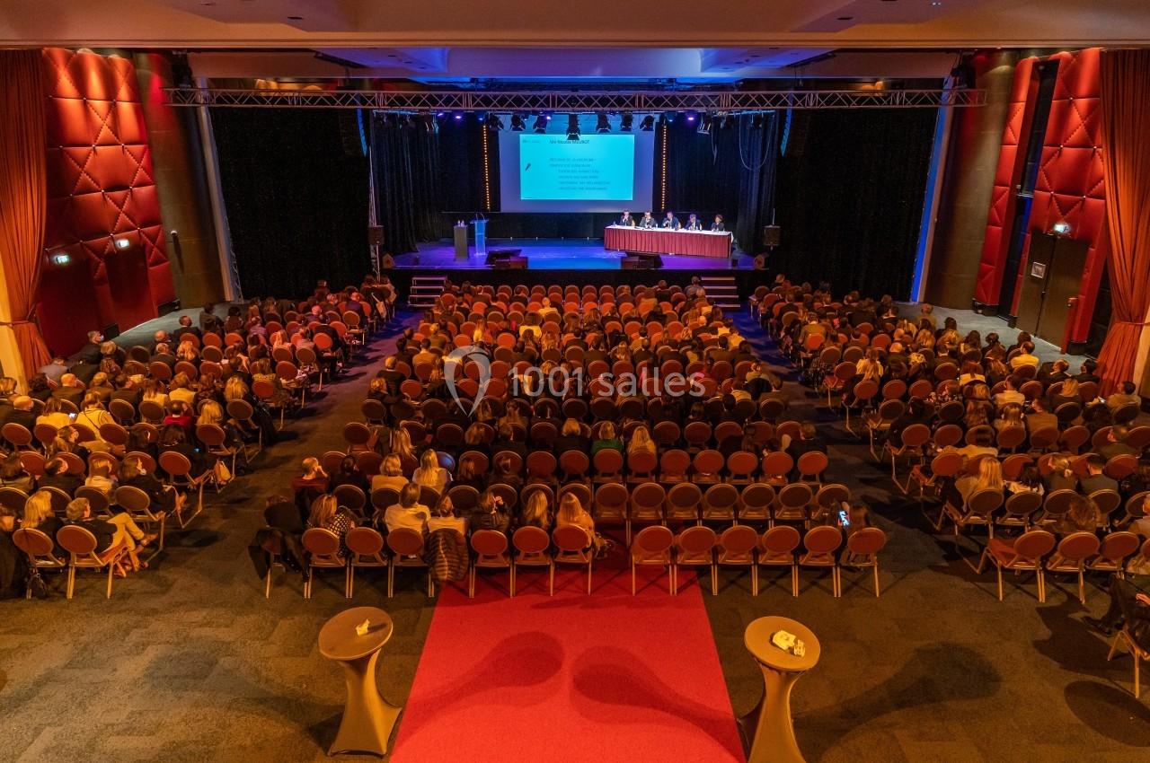 Salle de conférence avec un public nombreux, une scène éclairée et un écran projetant une présentation.