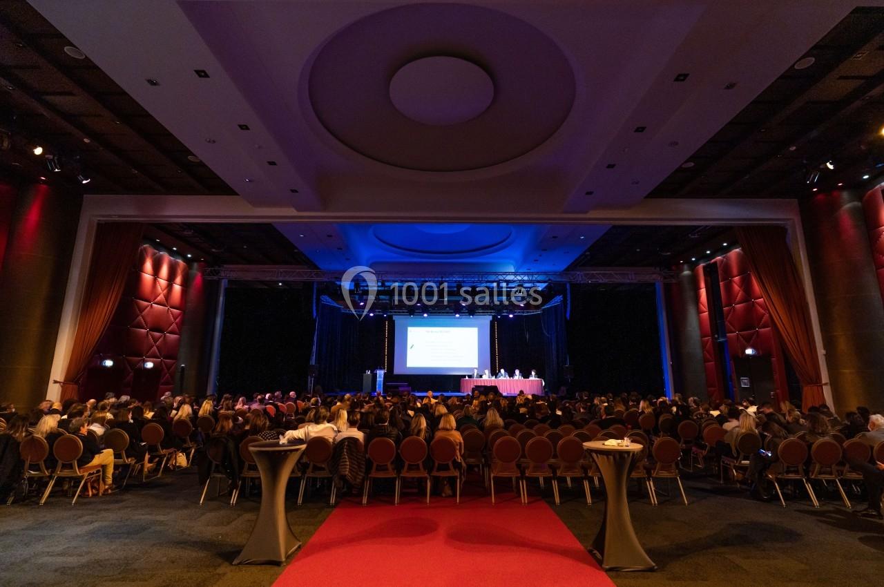 Salle de conférence avec un public assis face à une scène éclairée et un écran de présentation.