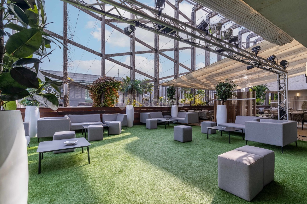 Espace extérieur aménagé avec des sièges modernes, du gazon artificiel et des plantes sous une structure lumineuse.