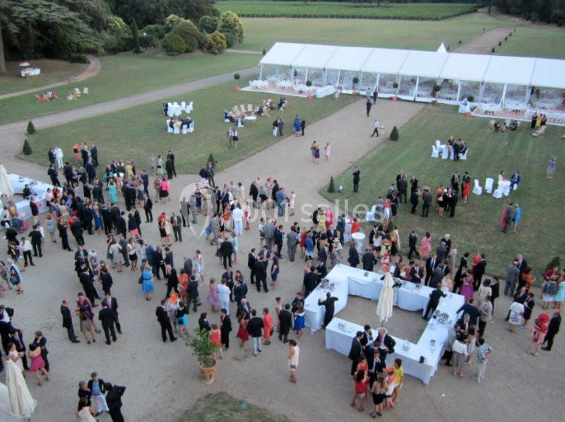 Vue aérienne d'un événement en plein air avec des invités rassemblés autour de tables et d'une tente blanche dans un parc.