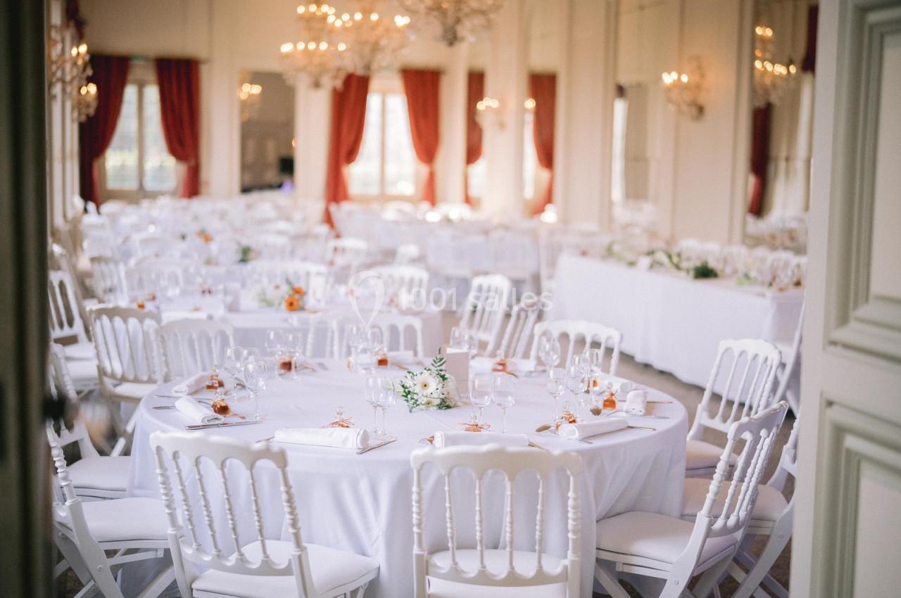 Salle de réception élégante avec des tables rondes dressées, nappes blanches et décorations florales.