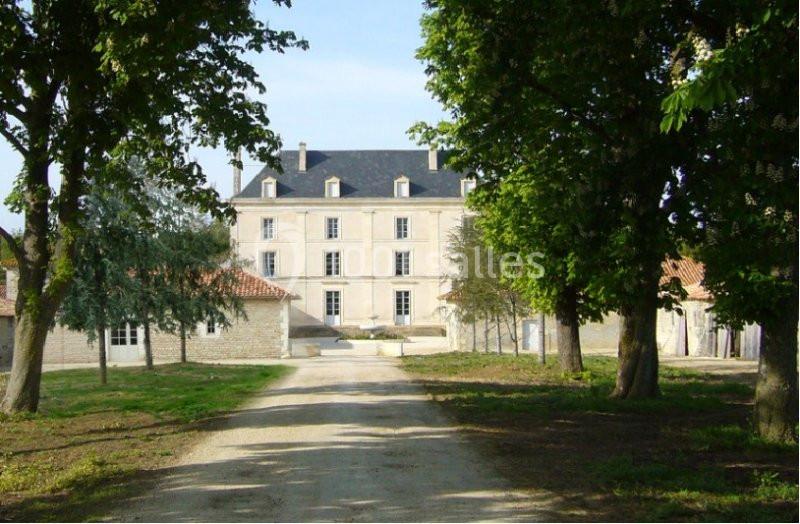 Allée bordée d'arbres menant à un grand bâtiment en pierre de style classique avec toit en ardoise.