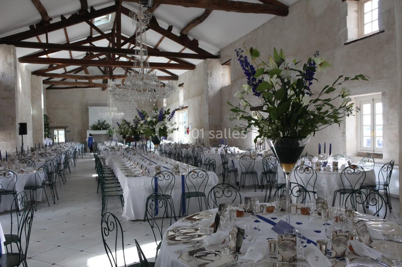 Grande salle de réception lumineuse avec tables dressées, chaises en fer forgé et décorations florales élégantes.