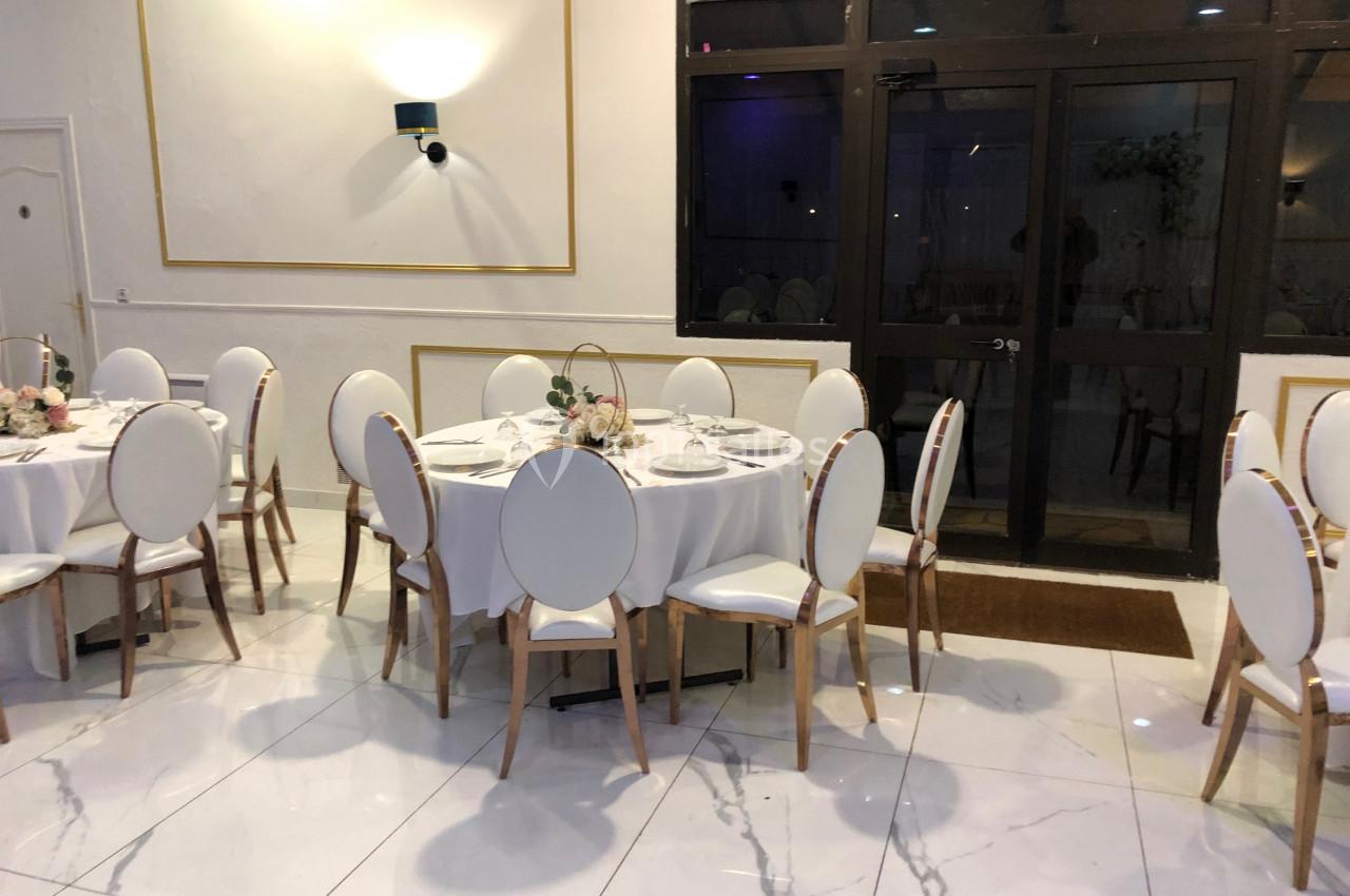Salle de réception avec tables rondes dressées, chaises blanches et décoration florale, sol en marbre blanc.