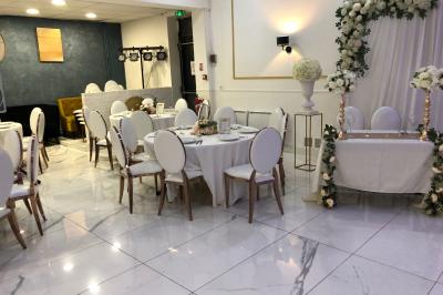Salle décorée avec des tables rondes dressées, nappes blanches, chaises élégantes et centre de table floral.