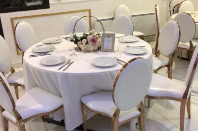Salle décorée avec des tables rondes dressées, nappes blanches, chaises élégantes et centre de table floral.