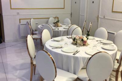 Salle décorée avec des tables rondes dressées, nappes blanches, chaises élégantes et centre de table floral.