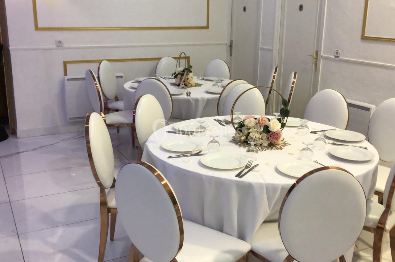 Salle élégante avec tables rondes dressées, nappes blanches, chaises assorties et centres de table floraux.