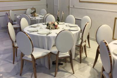 Salle décorée avec des tables rondes dressées, nappes blanches, chaises élégantes et centre de table floral.