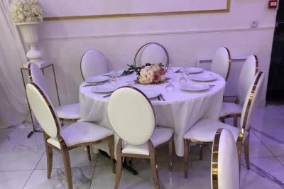 Salle décorée avec des tables rondes dressées, nappes blanches, chaises élégantes et centre de table floral.