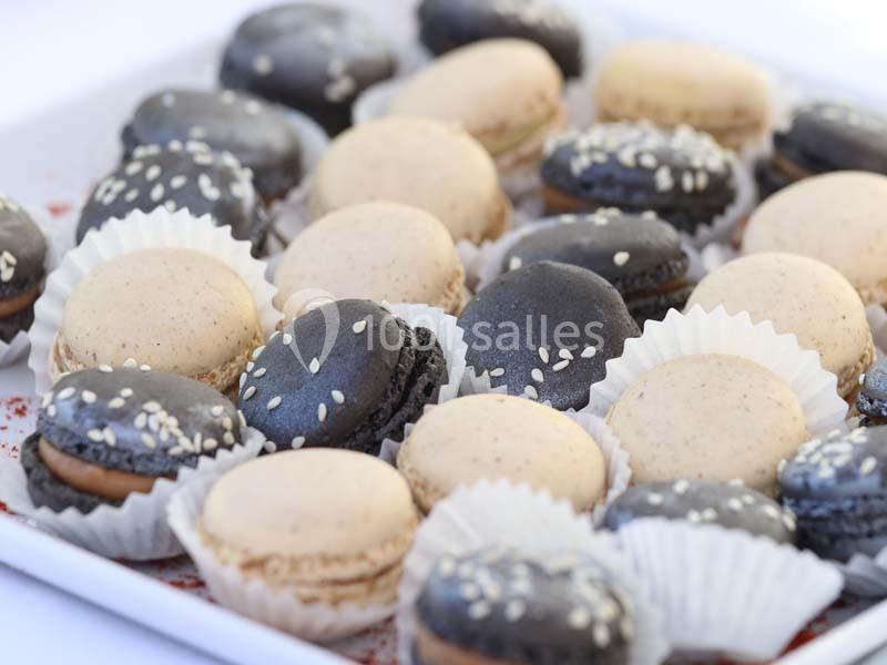 Plateau de macarons noirs et beiges garnis, certains décorés de graines de sésame, présentés dans des caissettes en papier.
