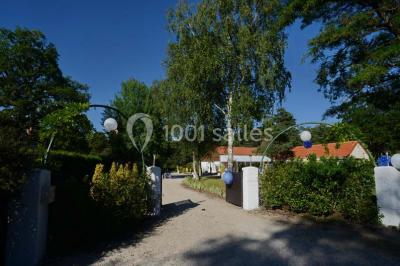 Miniature Location salle Arbonne-la-Forêt (Seine-et-Marne) - Le Domaine du Rocher #24 Allée gravillonnée bordée de verdure et de plantes, menant à une entrée avec des arches blanches sous un ciel dégagé.