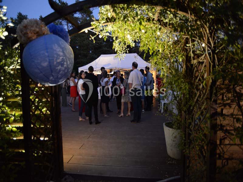 Groupe de personnes rassemblées en soirée dans un jardin éclairé, vu à travers une arche ornée de végétation.