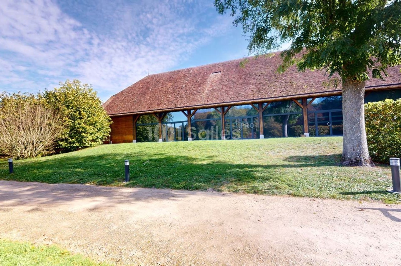 Bâtiment à toit en tuiles entouré de verdure, avec une façade vitrée et un chemin en premier plan.