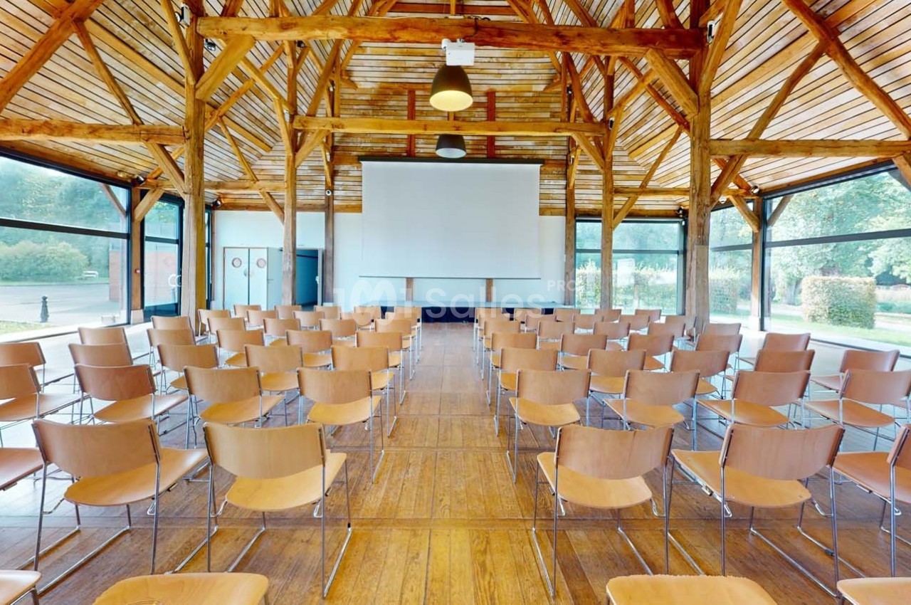 Salle de conférence lumineuse avec des chaises disposées face à un écran de projection, entourée de grandes baies vitrées.