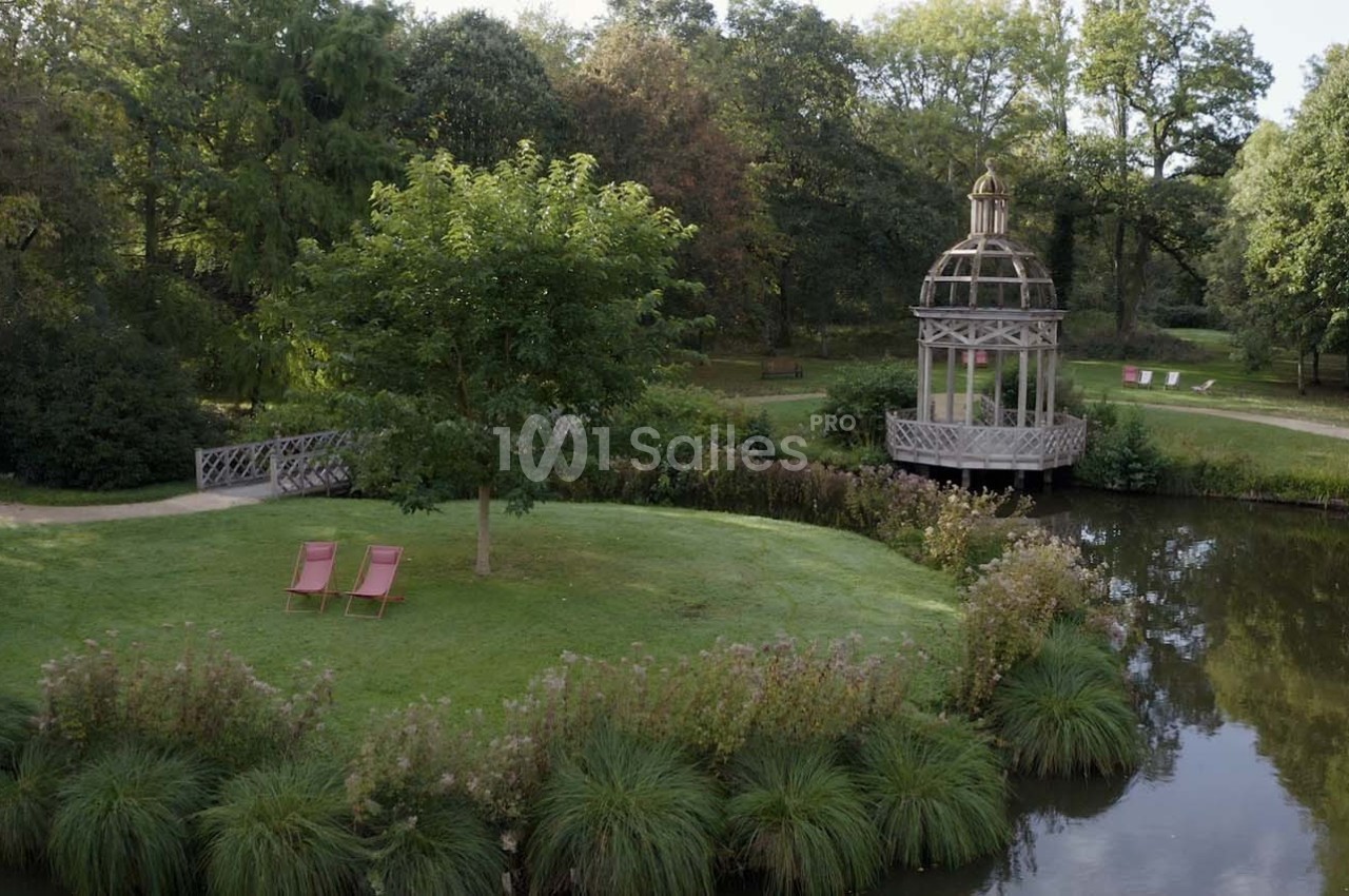 Un jardin verdoyant avec un kiosque en bois près d'un étang et deux chaises longues sur une pelouse.