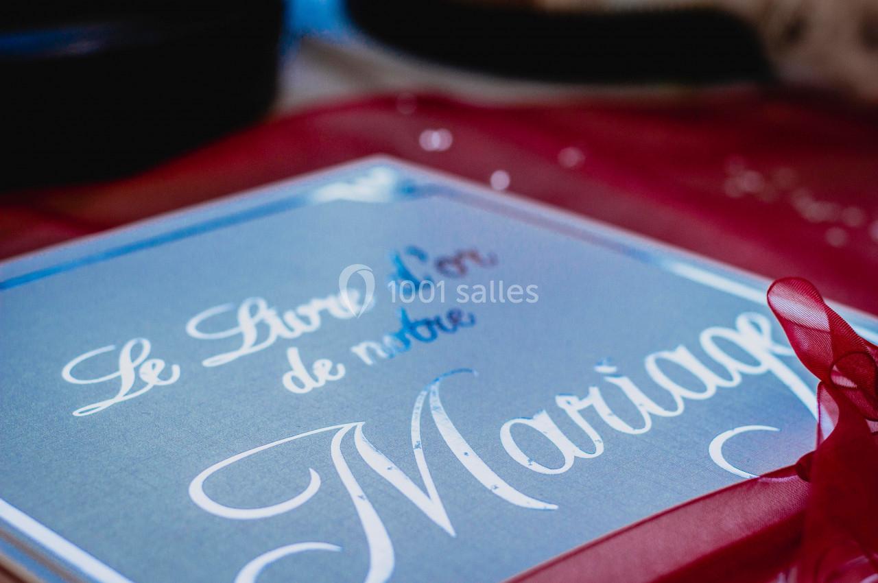 Livre d'or de mariage avec une couverture décorative et un ruban rouge posé sur une table.