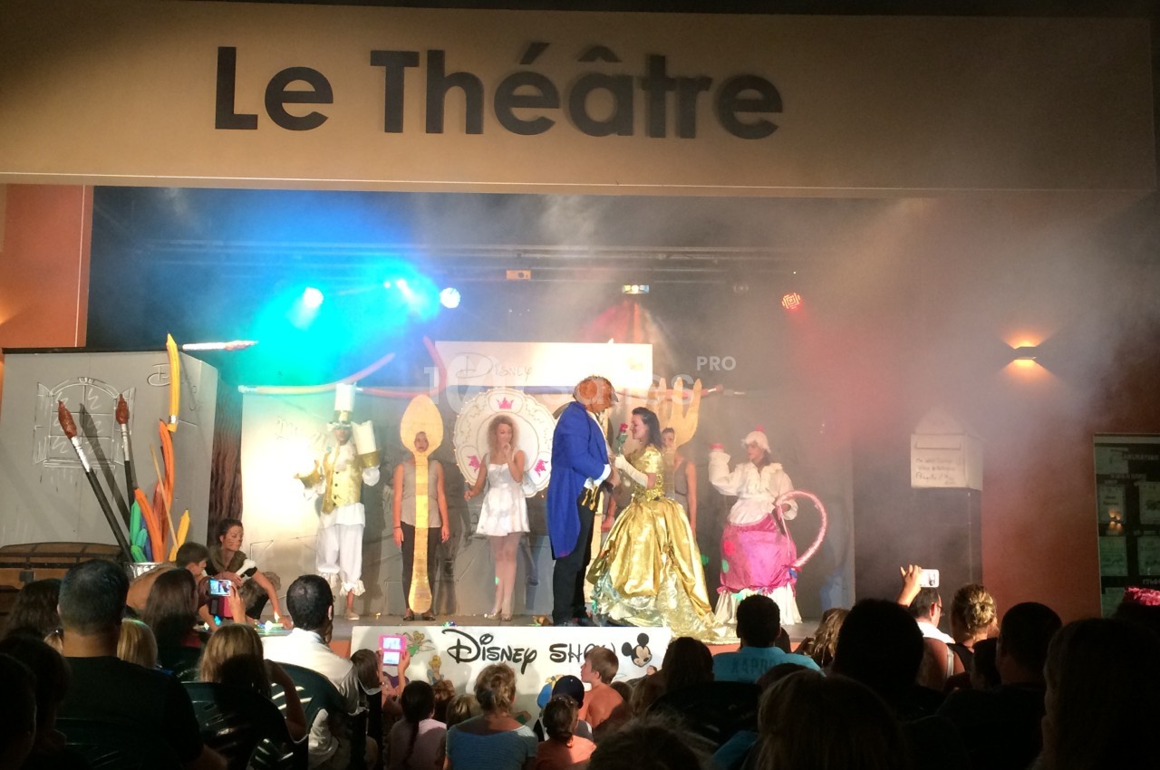 Spectacle sur scène avec des acteurs costumés devant un public, sous une enseigne indiquant ’Le Théâtre’.