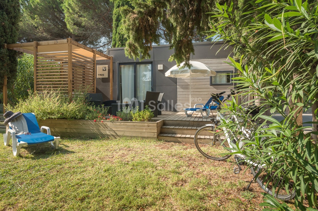 Terrasse en bois avec salon de jardin, transats, vélos et végétation environnante devant une habitation moderne.