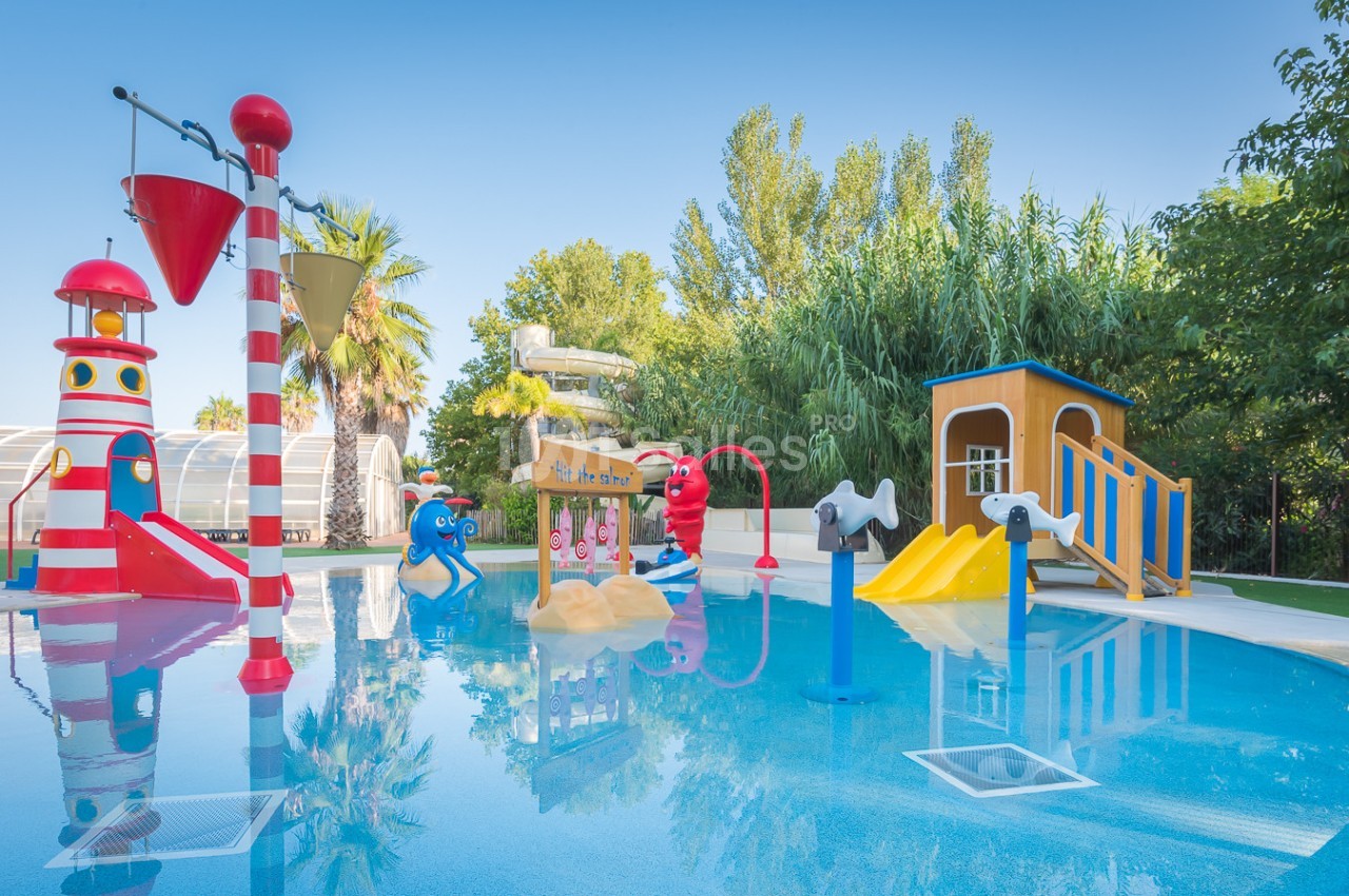 Aire de jeux aquatique colorée avec toboggans, jets d'eau et structures ludiques entourée de végétation.