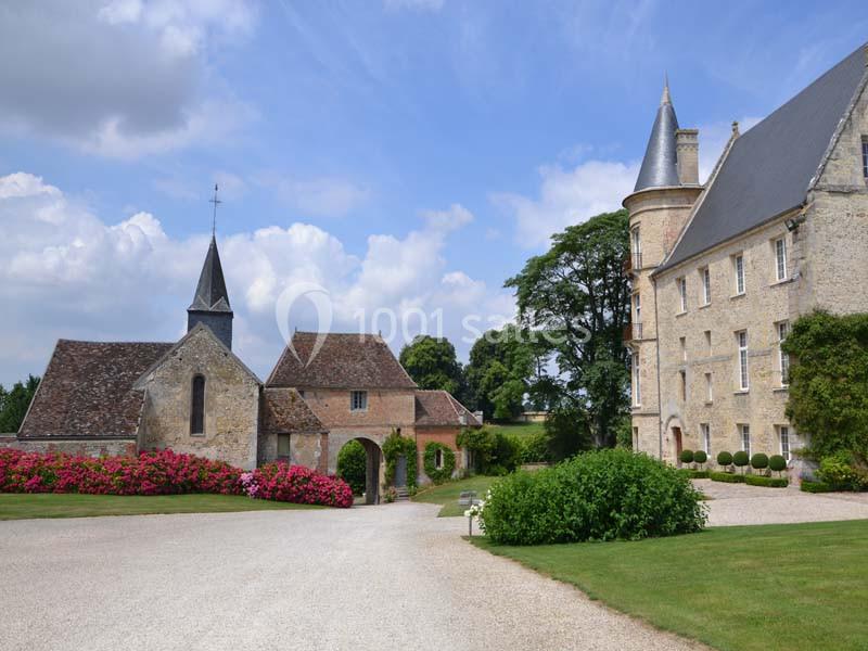 Vue d'un domaine avec une chapelle, un bâtiment en pierre, une allée gravillonnée et des jardins fleuris.