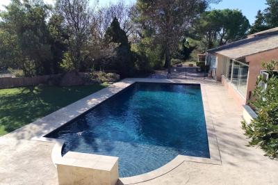 Vue aérienne d'une maison avec toit en tuiles, piscine rectangulaire et jardin arboré dans un cadre rural.