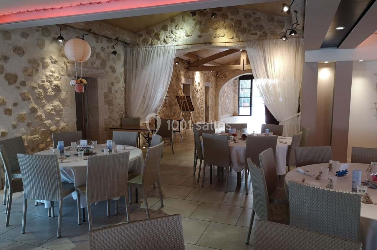 Salle de réception avec murs en pierre, tables rondes dressées et rideaux blancs créant une ambiance chaleureuse.