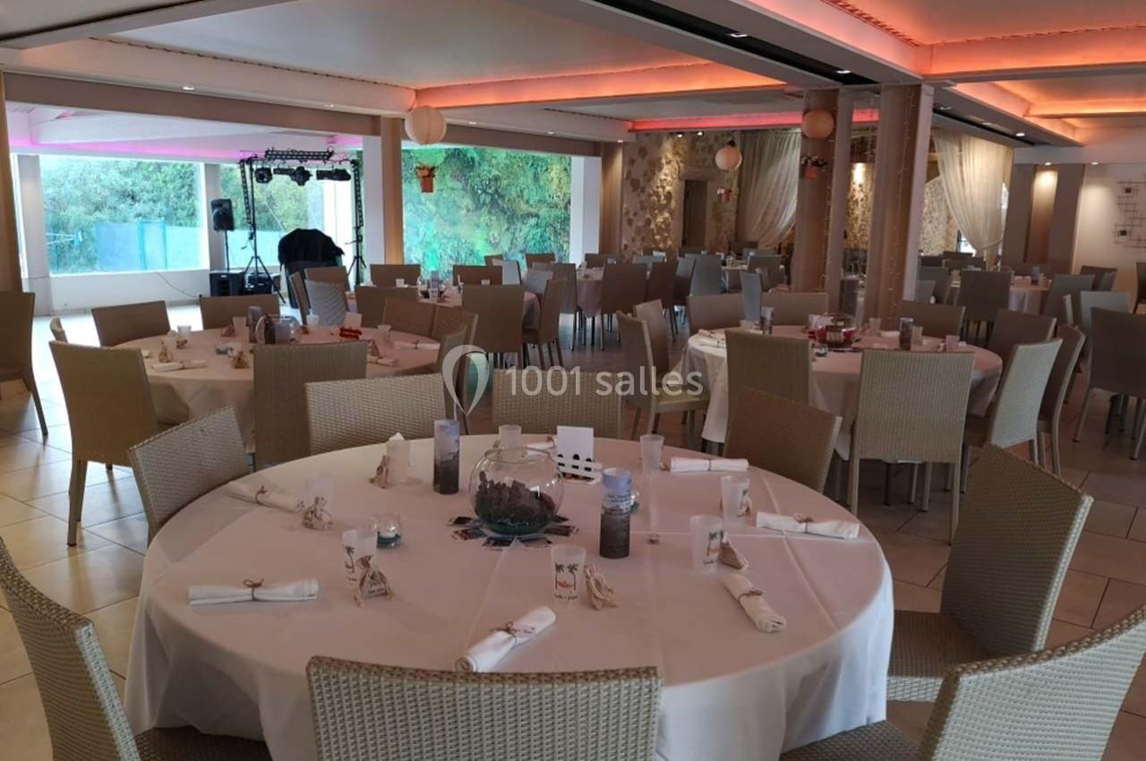 Salle de réception lumineuse avec tables rondes dressées, chaises en osier et décorations sobres.