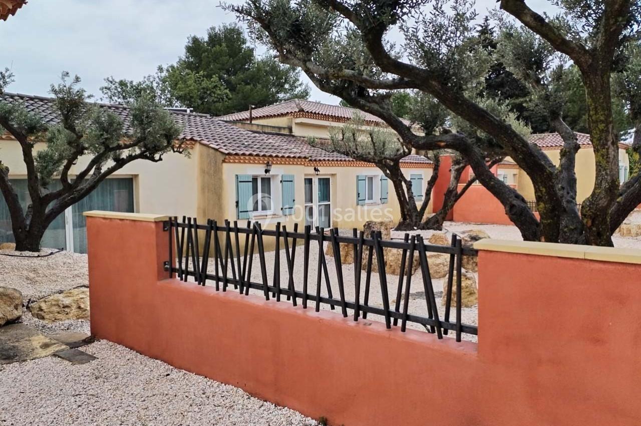 Maisons de plain-pied avec façades colorées, entourées d'oliviers et de graviers, séparées par une clôture métallique.