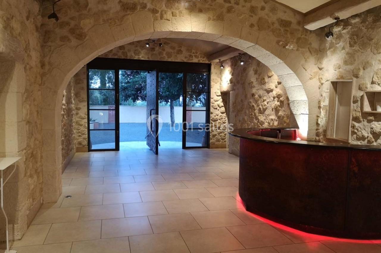 Salle avec murs en pierre, comptoir arrondi éclairé en rouge et grande ouverture vitrée donnant sur l'extérieur.