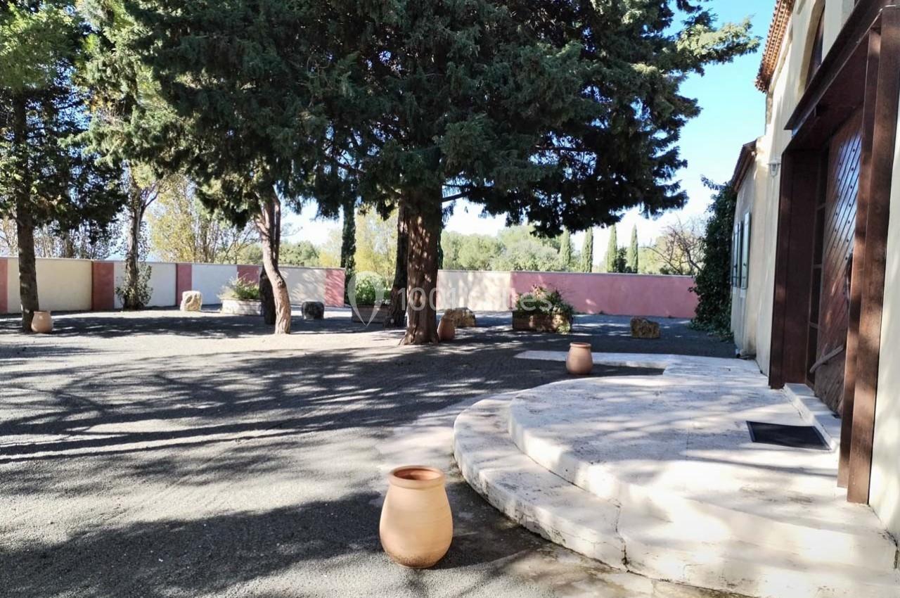 Cour extérieure ombragée avec des arbres, des pots en terre cuite et des marches en pierre près d'un bâtiment.