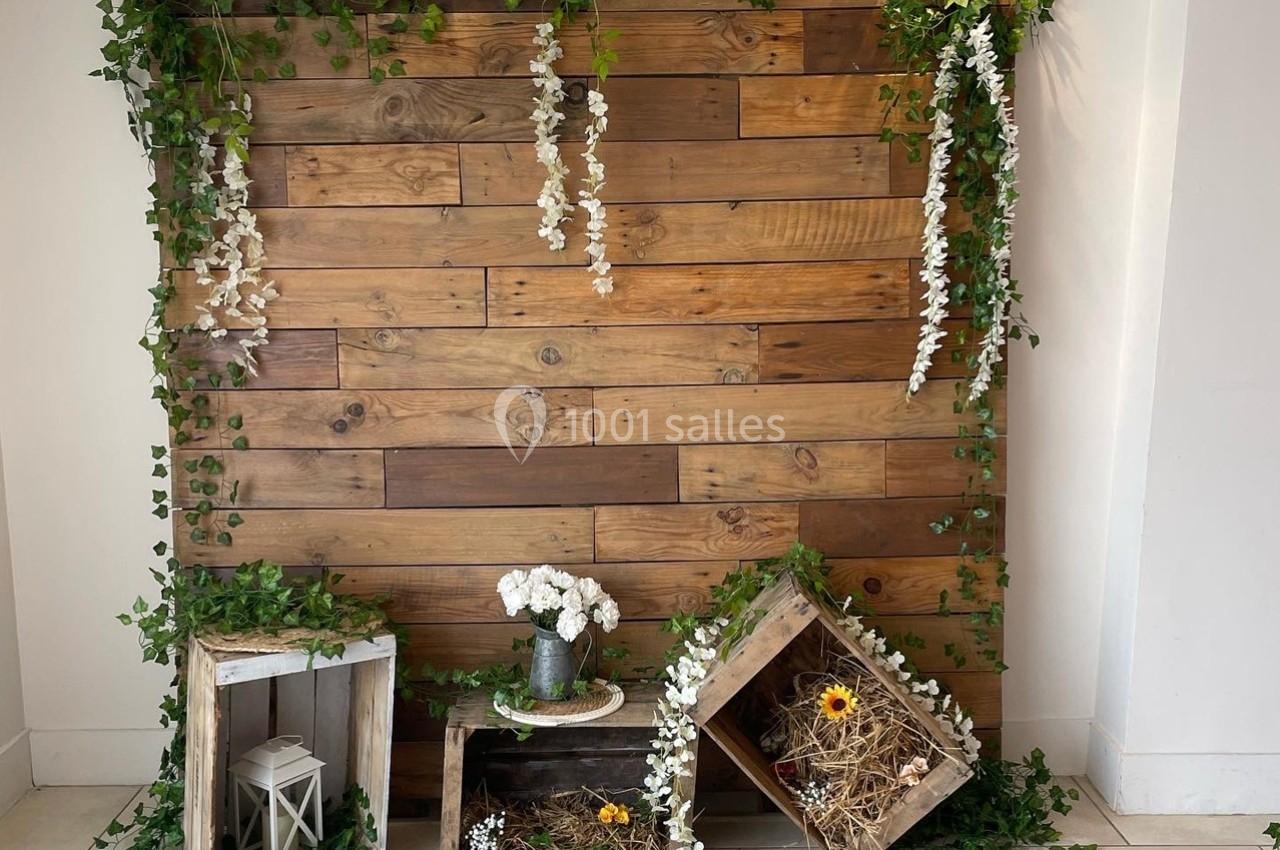 Mur en bois décoré de plantes grimpantes, caisses en bois contenant des fleurs et des éléments naturels.