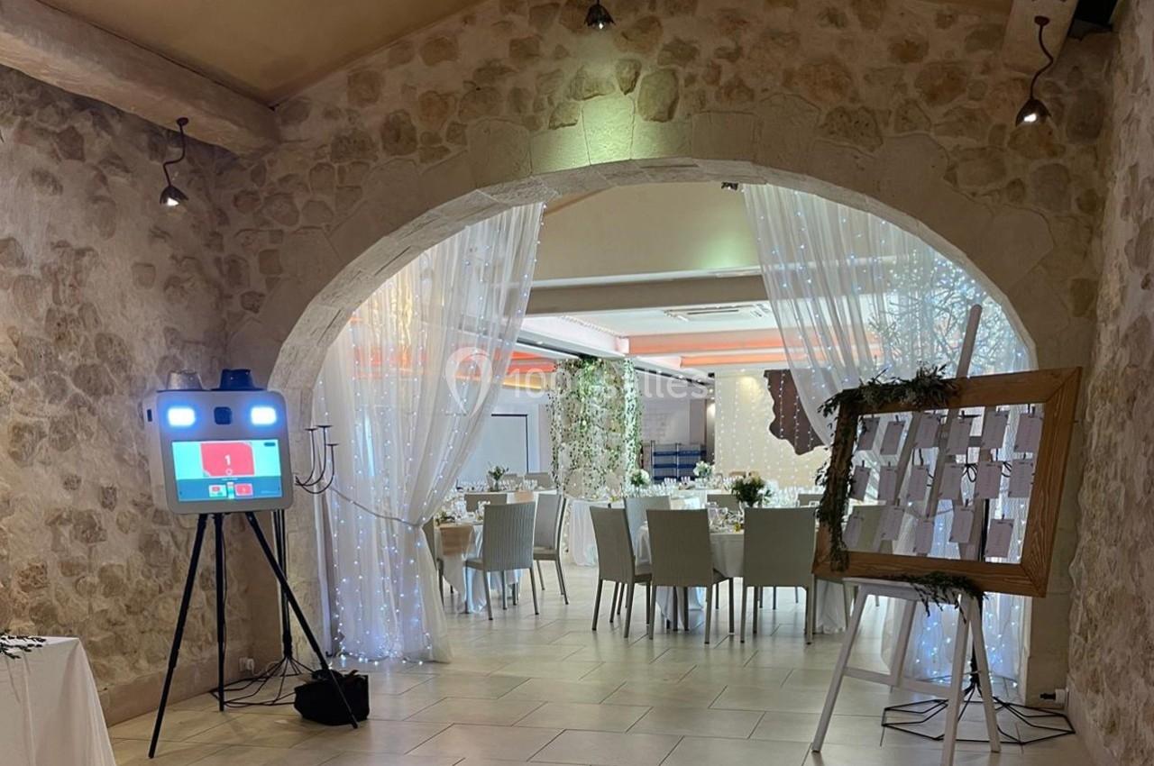 Salle de réception décorée avec des tables dressées, un plan de table sur chevalet et un photobooth lumineux.