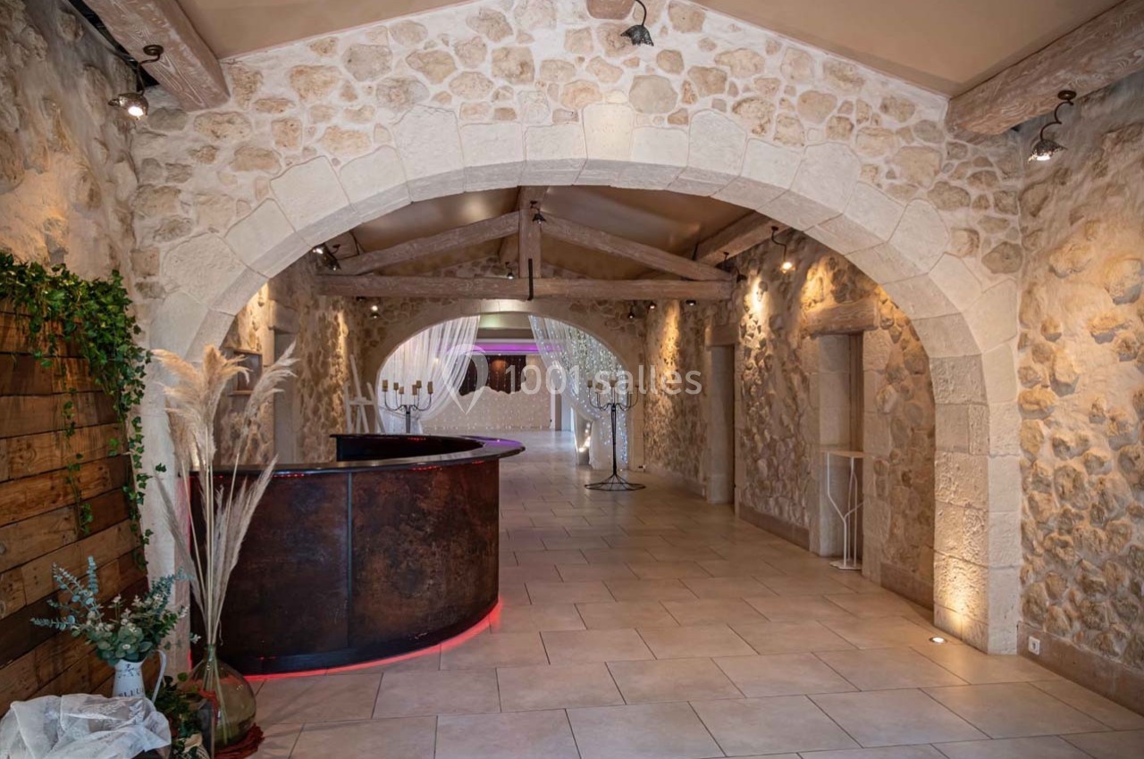 Salle en pierre avec un comptoir arrondi, des arches en pierre, un sol carrelé et une décoration végétale.