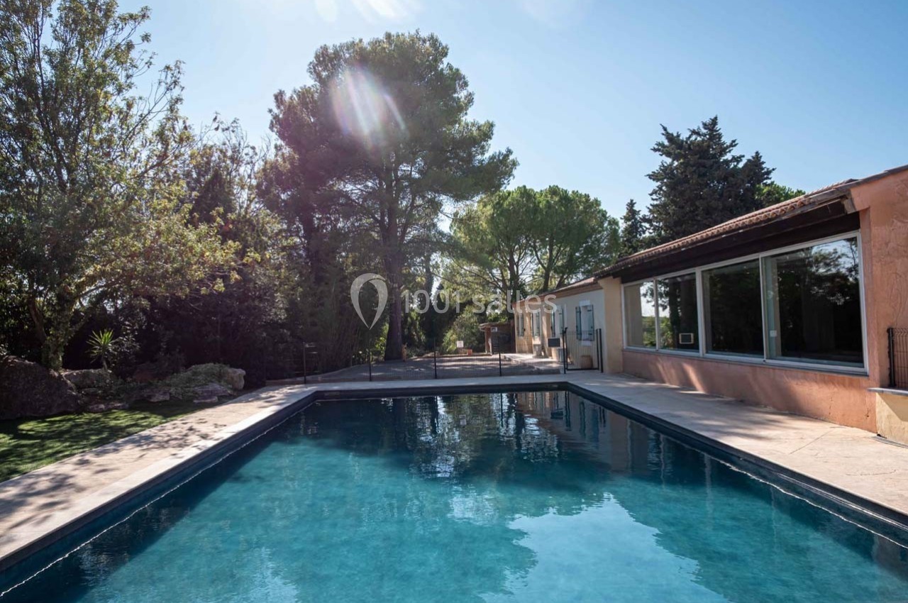 Piscine extérieure entourée de végétation et bordée d'une maison avec de grandes baies vitrées.