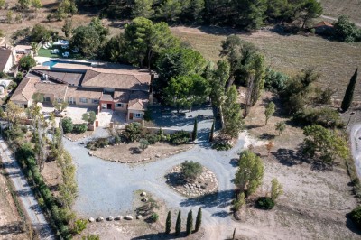 Vue aérienne d'une maison avec toit en tuiles, piscine rectangulaire et jardin arboré dans un cadre rural.