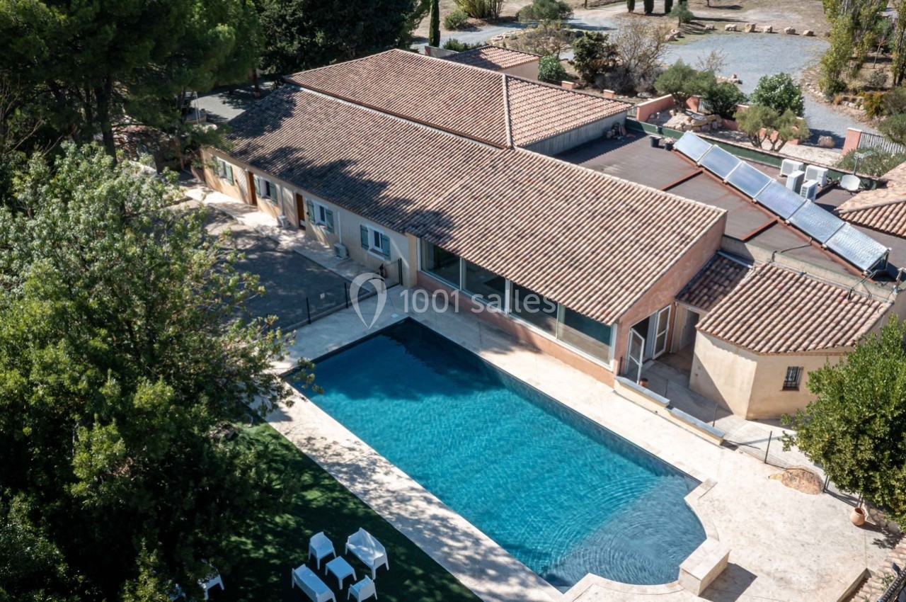 Vue aérienne d'une maison avec toit en tuiles, piscine rectangulaire et jardin arboré.