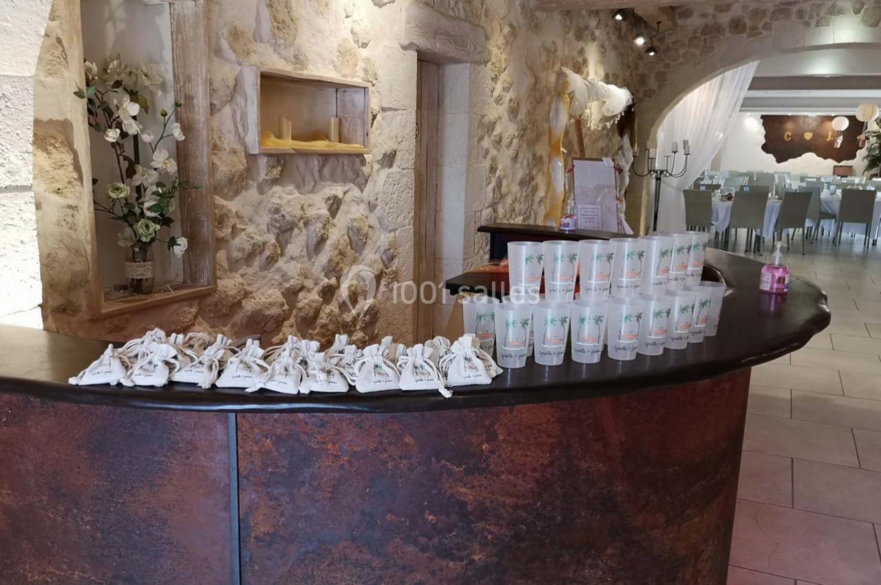 Comptoir en pierre avec des sachets en tissu et des gobelets alignés, dans une salle de réception en pierre apparente.