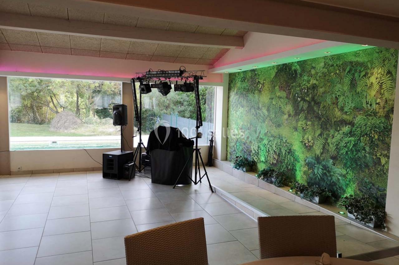 Salle lumineuse avec mur végétal, équipement audio et éclairage installé près d'une baie vitrée donnant sur un jardin.