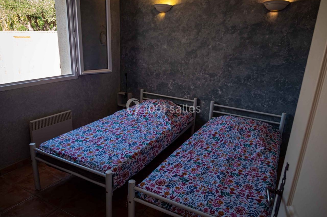 Deux lits simples avec des draps à motifs colorés dans une chambre sombre, éclairée par des appliques murales.