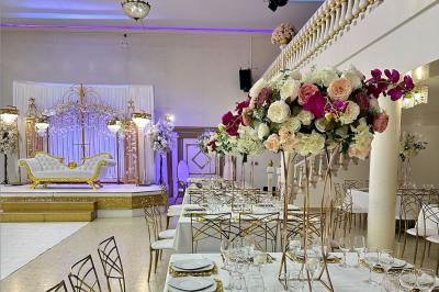 Salle de réception décorée avec des tables élégantes, des bouquets de fleurs et une estrade ornée d'un canapé doré.