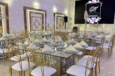 Salle de réception décorée avec des tables élégantes, des bouquets de fleurs et une estrade ornée d'un canapé doré.