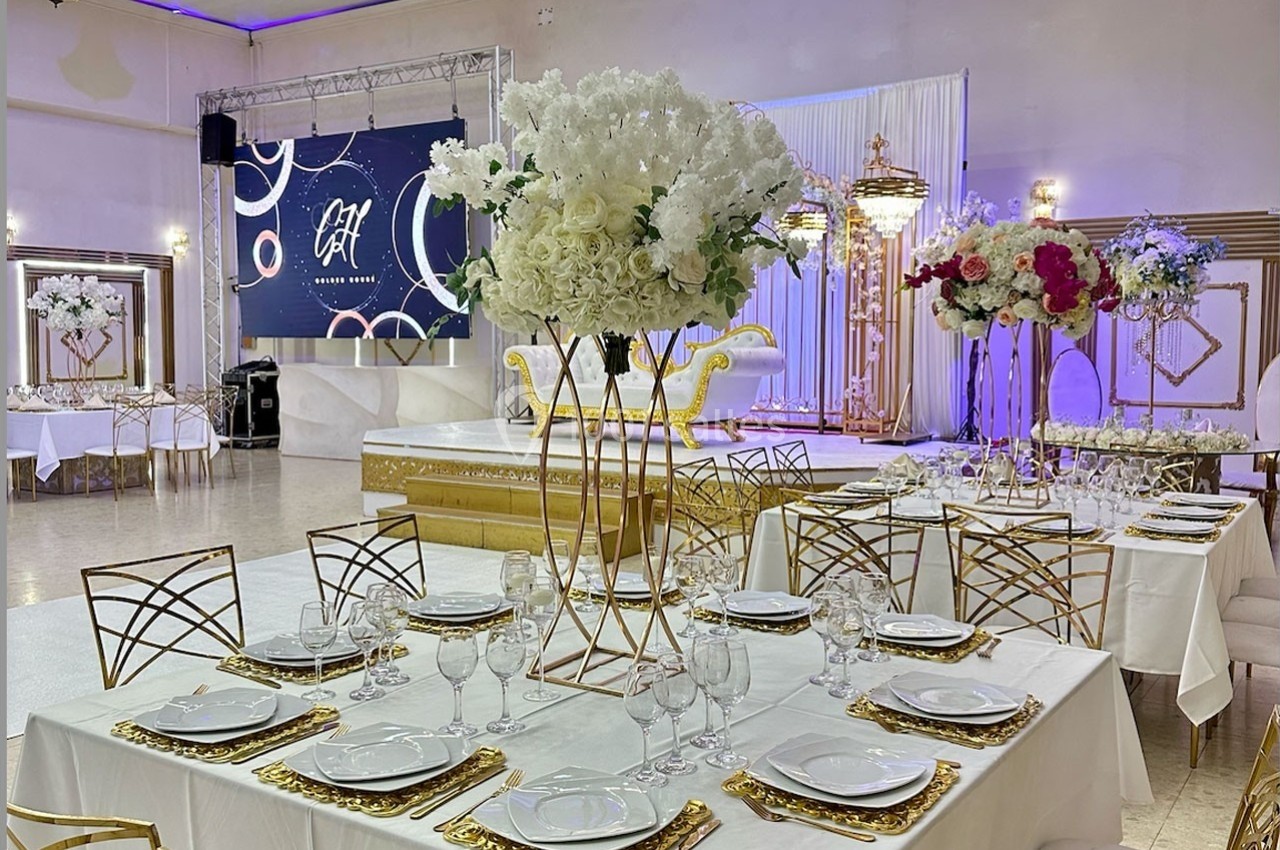 Salle de réception décorée avec des tables dressées, des centres de table floraux et une scène ornée en arrière-plan.